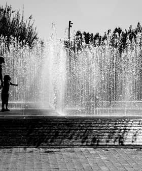 Silhouettes of children playing in a water fountain with water spraying in the background. - Olive Oil Times