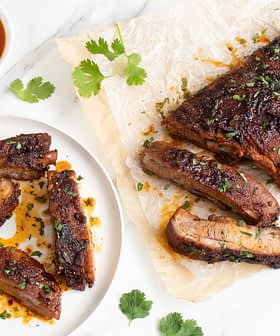 Plate of cooked pork ribs with a side of sauce and garnished with herbs. - Olive Oil Times