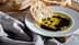 Slice of bread dipped in olive oil with balsamic vinegar on a white plate. - Olive Oil Times