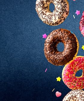 Four assorted donuts with chocolate, pink, and white icing, topped with sprinkles and colorful decorations. - Olive Oil Times