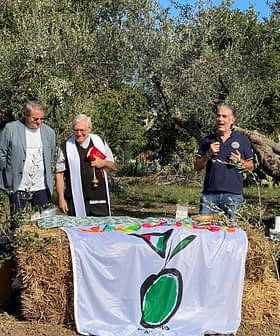 Four individuals speaking at an outdoor event with an olive-themed banner in front of them. - Olive Oil Times