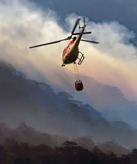 Helicopter flying over a mountainous area with a water bucket suspended below it. - Olive Oil Times