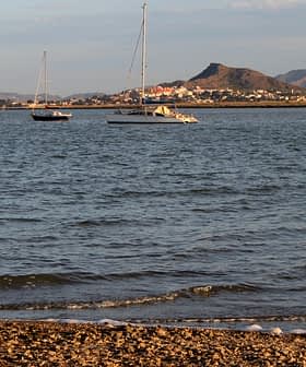Two sailboats anchored on calm water with mountains visible in the background. - Olive Oil Times