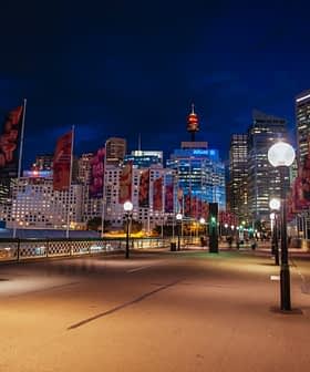 Night view of Sydney cityscape featuring illuminated buildings and decorative flags along a walkway. - Olive Oil Times