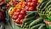 Baskets of cucumbers and tomatoes arranged in a market setting with vibrant colors. - Olive Oil Times