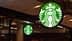 Illuminated Starbucks logo sign featuring a green background and white mermaid design. - Olive Oil Times