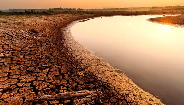 Dry, cracked earth along the edge of a river reflecting the sunset light. - Olive Oil Times