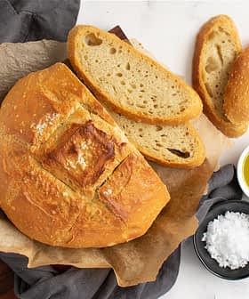 Round artisan bread loaf with slices, olive oil, and sea salt on a marble surface. - Olive Oil Times