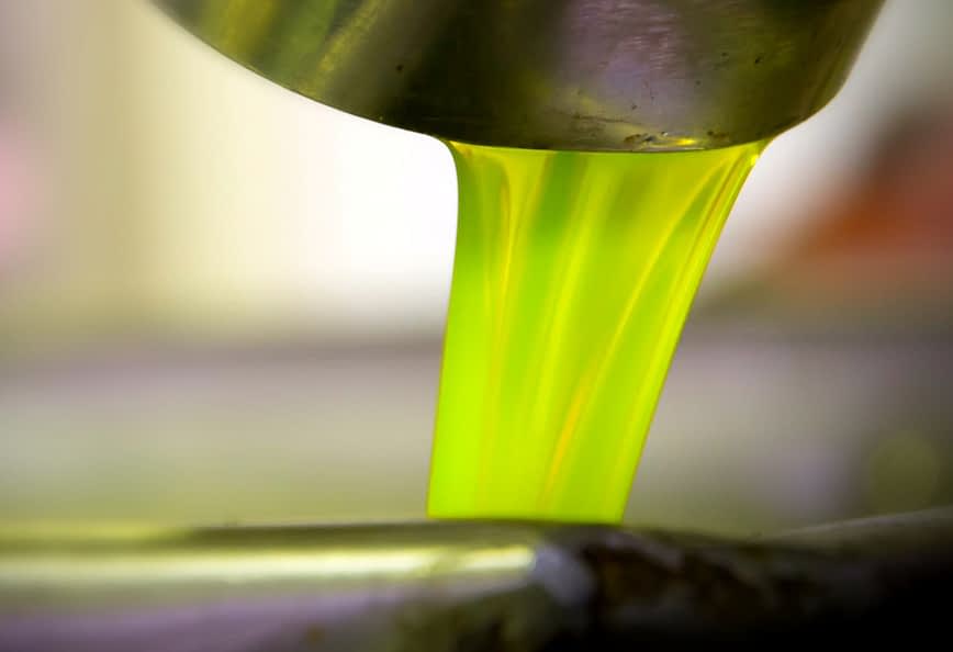 Bright green olive oil pouring from a metal container into a bowl. - Olive Oil Times