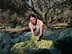 Woman holding freshly harvested olives while sitting on a green net in an olive grove. - Olive Oil Times