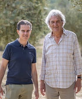 Two men standing in an olive grove, both smiling and dressed casually in light clothing. - Olive Oil Times