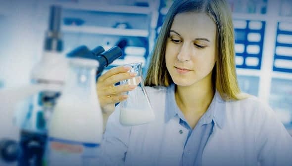 Female scientist examining a beaker containing a liquid in a laboratory setting. - Olive Oil Times