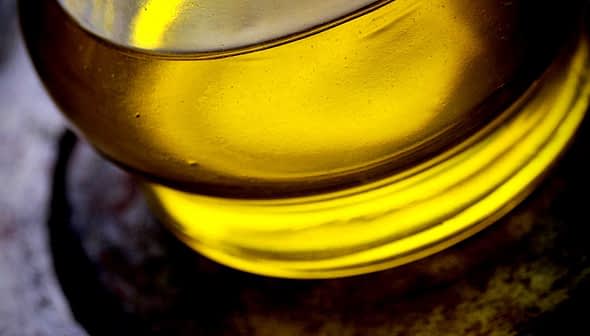 Close-up view of olive oil in a glass container with a yellow hue. - Olive Oil Times