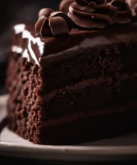 Slice of chocolate layer cake with chocolate frosting and decorative swirls on top. - Olive Oil Times