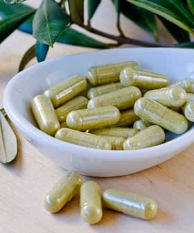 A white dish containing green herbal capsules, surrounded by leaves on a wooden surface. - Olive Oil Times