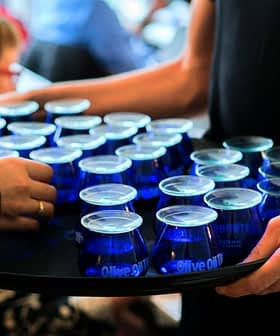 A tray holding multiple blue glasses filled with olive oil being served at an event. - Olive Oil Times