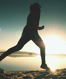 Silhouette of a person jogging along the shore of a lake during sunrise. - Olive Oil Times