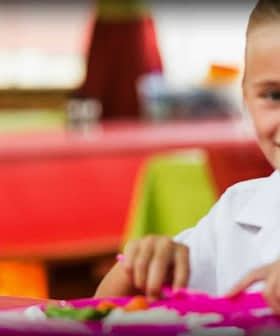Two children smiling while eating lunch at a colorful table in a dining area. - Olive Oil Times
