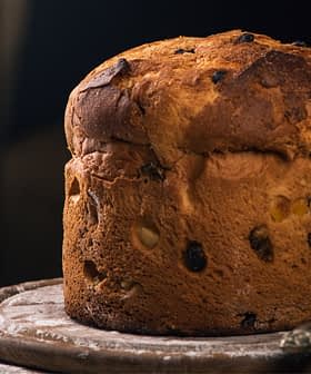 A round loaf of bread with a golden-brown crust and visible raisins on a wooden surface. - Olive Oil Times