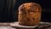 A round loaf of bread with a golden-brown crust and visible raisins on a wooden surface. - Olive Oil Times