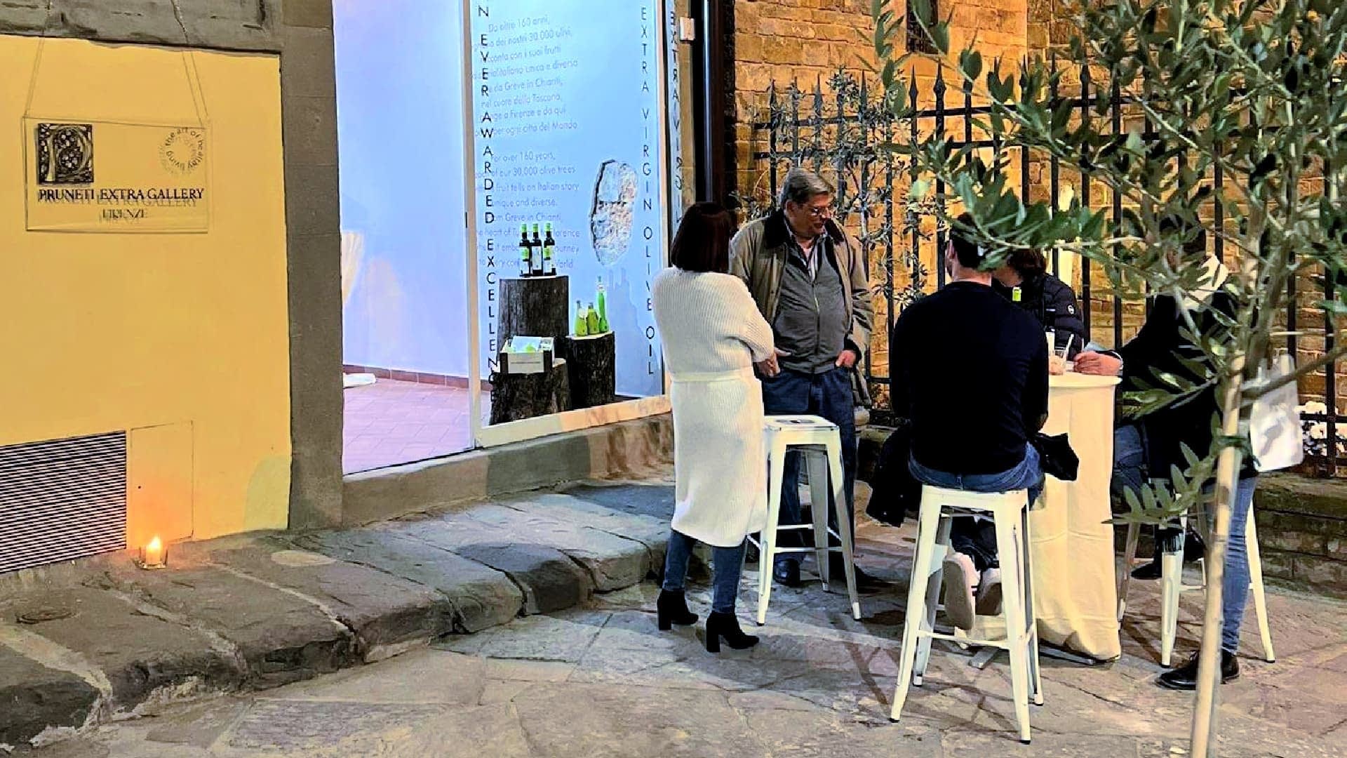 A group of four people gathered around a table outside an art gallery, engaged in conversation. - Olive Oil Times