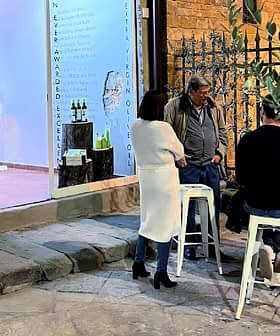 A group of four people gathered around a table outside an art gallery, engaged in conversation. - Olive Oil Times