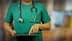 Healthcare professional in green scrubs using a tablet device while wearing a stethoscope. - Olive Oil Times