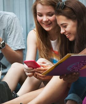 Four young individuals sitting together, sharing a moment while looking at a smartphone. - Olive Oil Times