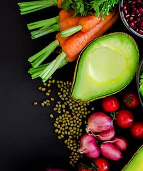 An assortment of fresh vegetables including carrots, celery, and avocado arranged on a dark surface. - Olive Oil Times