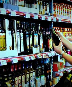 A woman examining a bottle of olive oil while shopping in a grocery store aisle filled with various oils. - Olive Oil Times