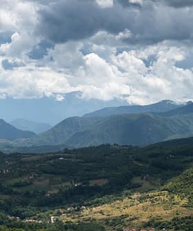 A panoramic view of mountains under a cloudy sky with varying shades of green vegetation. - Olive Oil Times