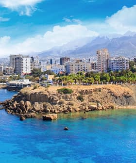 Coastal view featuring a city skyline with mountains in the background and clear blue water. - Olive Oil Times