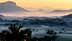 A misty landscape featuring mountains and valleys during sunrise with soft light and fog. - Olive Oil Times
