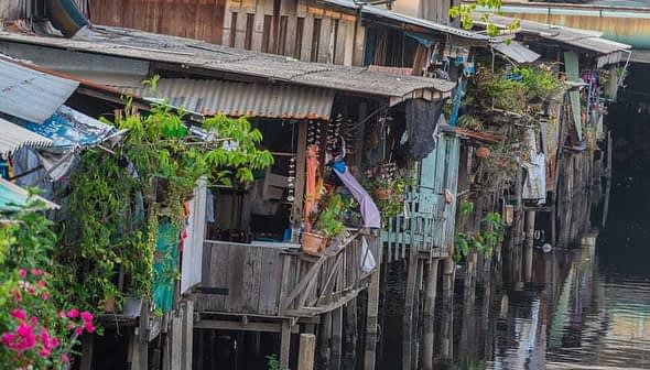 Wooden houses on stilts along a waterway, featuring plants and clothes hanging outside. - Olive Oil Times