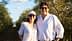 A man and woman smiling while standing in an olive grove under a clear sky. - Olive Oil Times