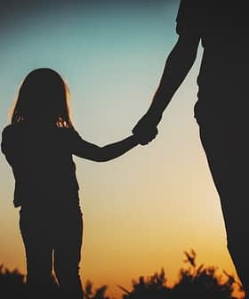 Silhouette of an adult and a child holding hands against a sunset background. - Olive Oil Times