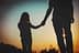 Silhouette of an adult and a child holding hands against a sunset background. - Olive Oil Times