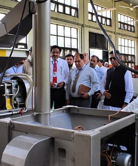 Group of individuals observing an oil extraction machine during a demonstration in a factory setting. - Olive Oil Times