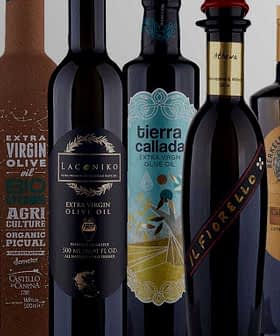 A collection of olive oil bottles with distinct labels and designs arranged in a row. - Olive Oil Times