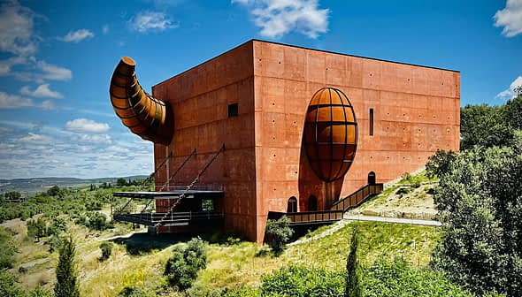 A large, red architectural building with a prominent spherical and cylindrical design element. - Olive Oil Times