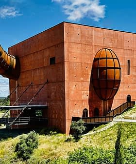 A large, red architectural building with a prominent spherical and cylindrical design element. - Olive Oil Times