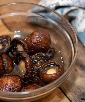 A glass bowl containing soaked mushrooms in liquid, placed on a wooden surface. - Olive Oil Times