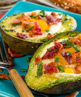Baked avocado halves filled with egg, topped with bacon bits and chives on a blue plate. - Olive Oil Times