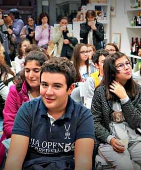 A group of young individuals seated in a room, some smiling and others engaged in conversation. - Olive Oil Times