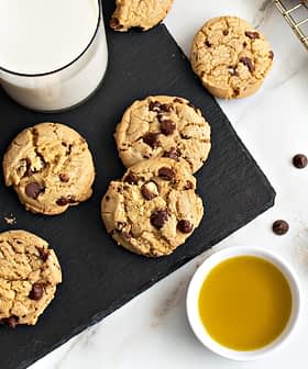 Plate of chocolate chip cookies next to a glass of milk and a bowl of olive oil. - Olive Oil Times