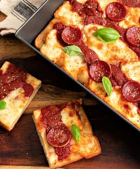 A rectangular pepperoni pizza topped with tomato sauce and fresh basil leaves, served in a baking tray. - Olive Oil Times