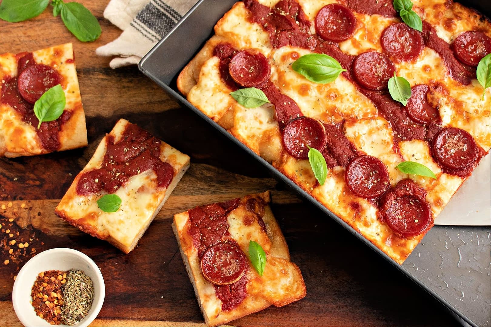 A rectangular pepperoni pizza topped with tomato sauce and fresh basil leaves, served in a baking tray. - Olive Oil Times