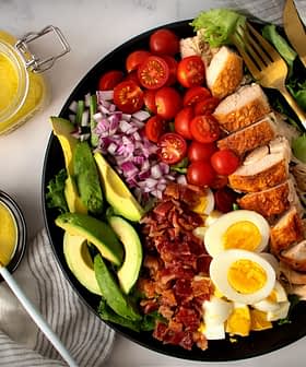 A colorful salad featuring grilled chicken, avocado, cherry tomatoes, and hard-boiled eggs on a black plate. - Olive Oil Times