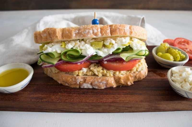 A sandwich made with whole grain bread, filled with egg salad, cucumbers, tomatoes, and pickles. - Olive Oil Times