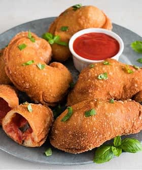 A plate of fried dough pieces garnished with green herbs and served with a small bowl of tomato sauce. - Olive Oil Times